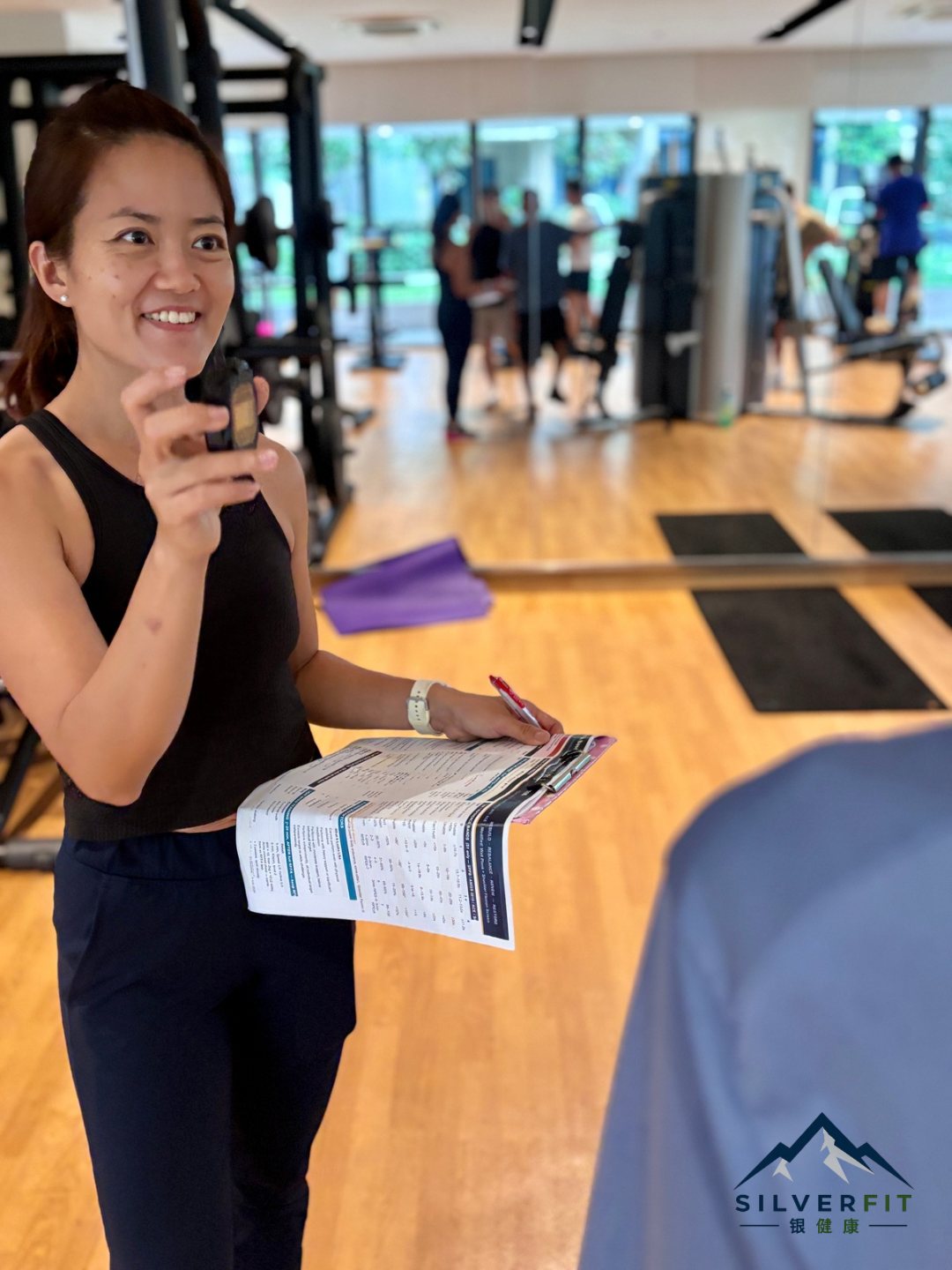 Yvonne Ong holding a stopwatch and coaching programme sheet in the gym