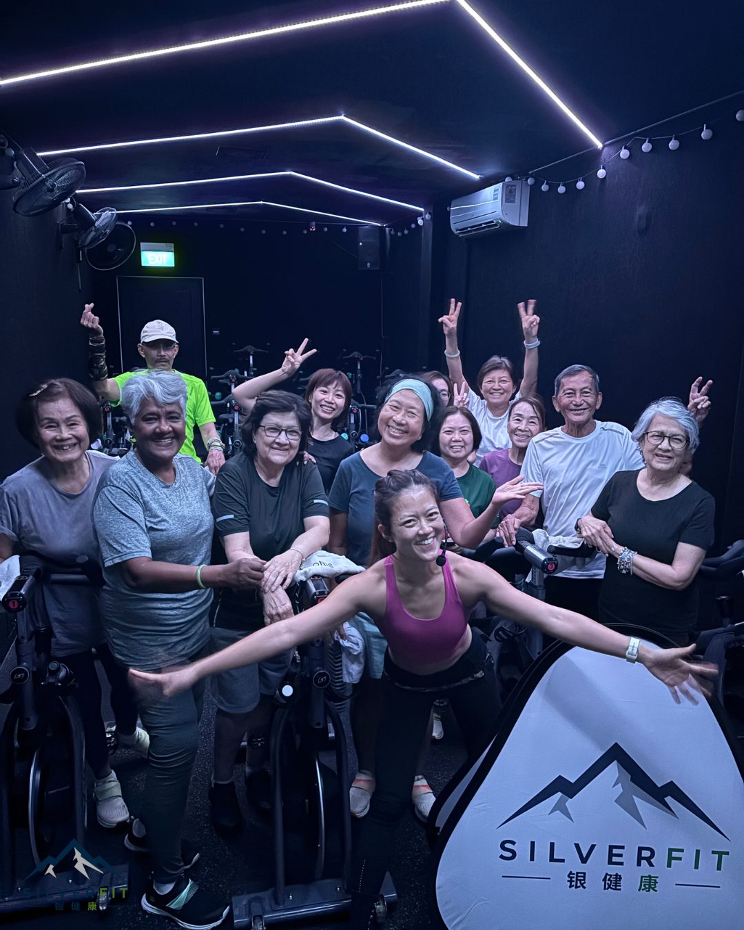 A full class of SilverFit seniors and volunteers smiling together after a Ride Beside Them indoor cycling session